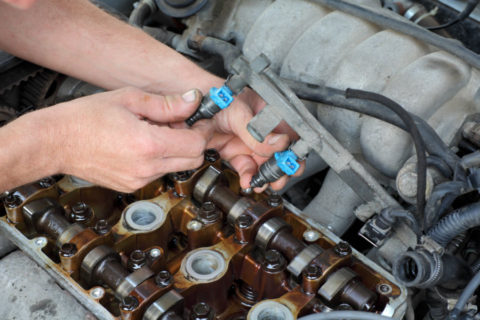 Image of a mechanic holding a set of fuel injectors on an engine block